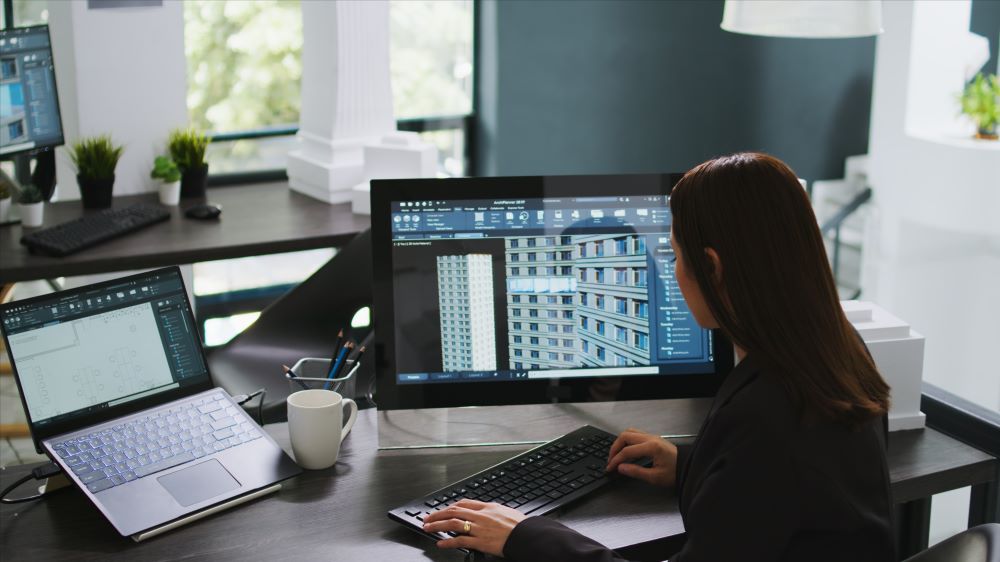 Profissional utiliza software BIM em computador com modelo 3D de edifício, representando serviços de modelagem e projeto digital.